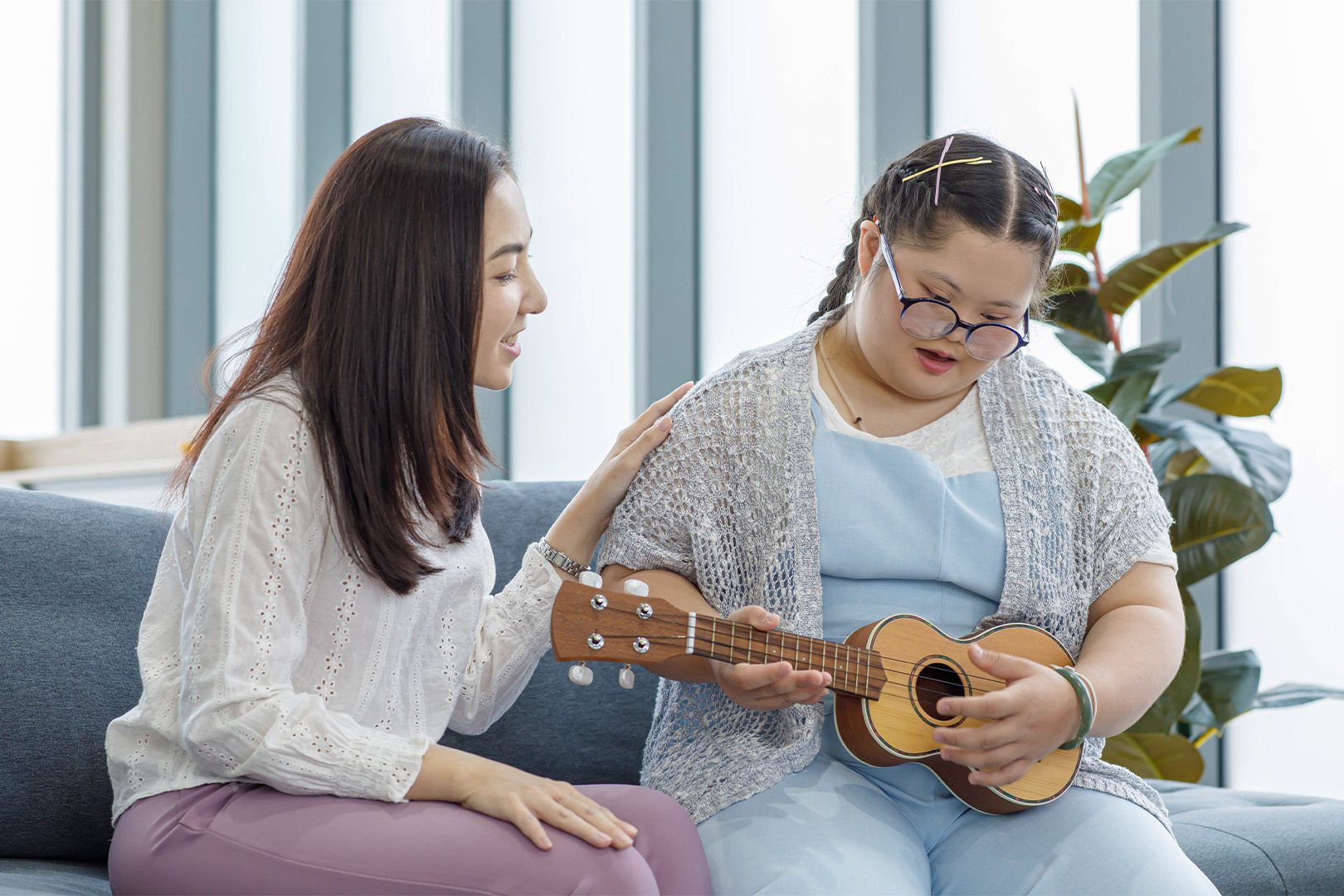 Asian woman teaching a young girl with down syndrome to play Ukulele musical instrument